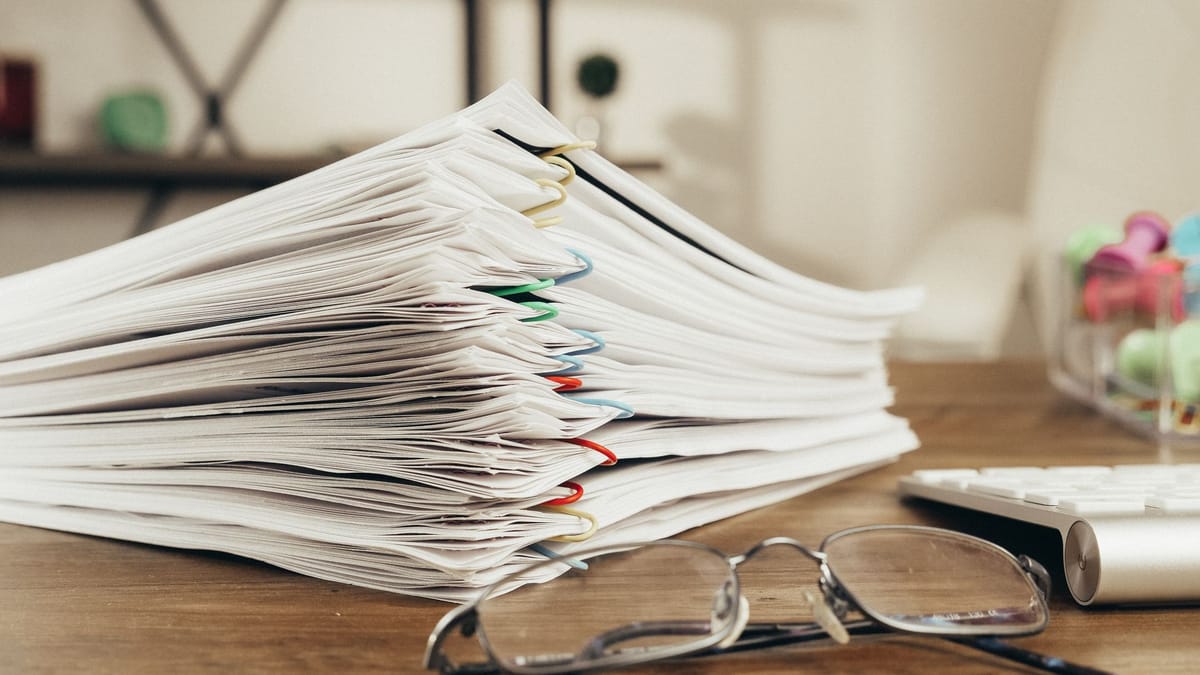 A stack of paper-clipped documents beside eyeglasses and a pen.
