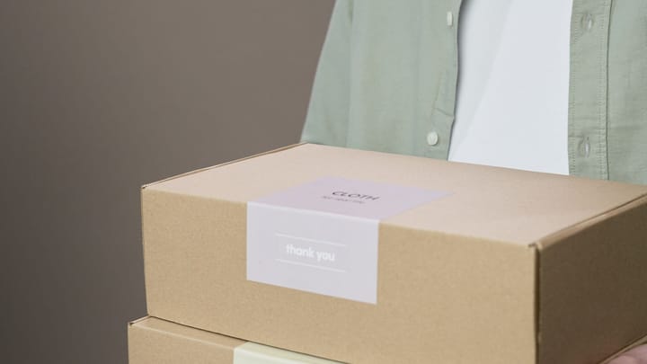 A person carries two cardboard boxes with visible labels on the front.