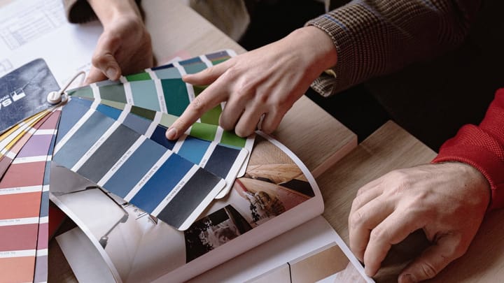 Two people point at blue and green color swatches in a design book.