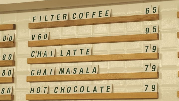 A cafe wall menu lists drink options and prices above a counter.