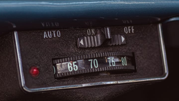 A close-up of a vintage dashboard control panel with labeled switches, dials, and a red indicator light.